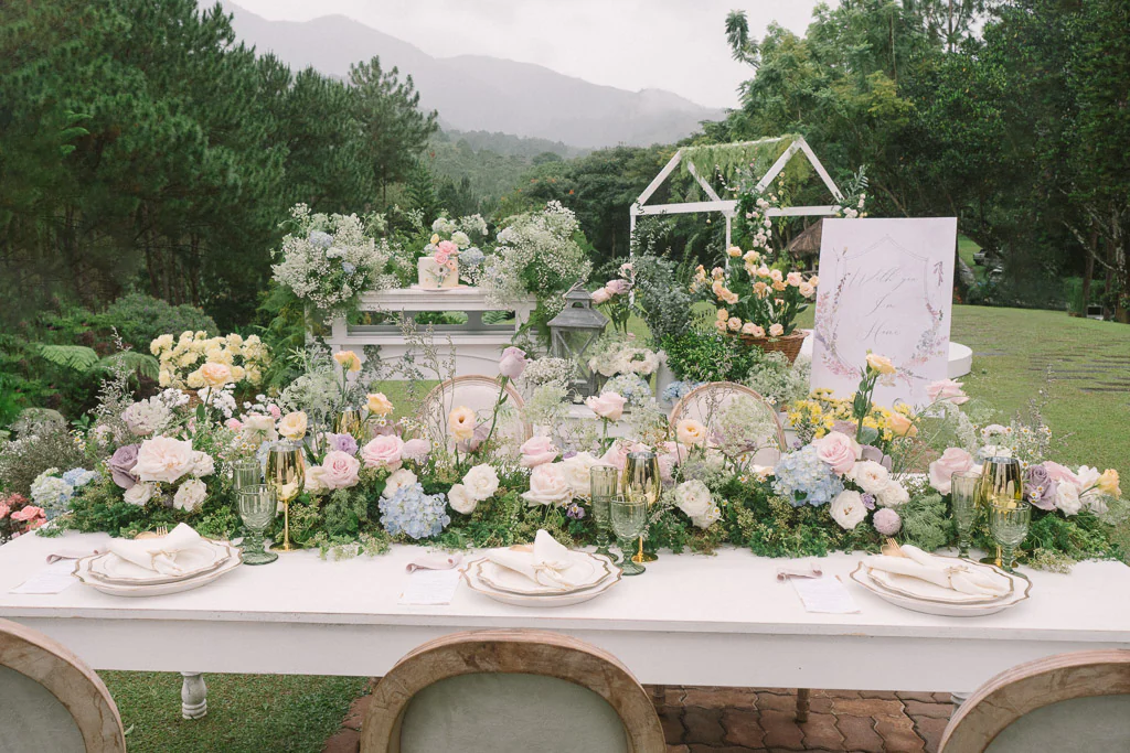 an outdoor 10th wedding anniversary reception with fine table setting and fresh floral centerpieces by Khim Cruz against a mountain backdrop