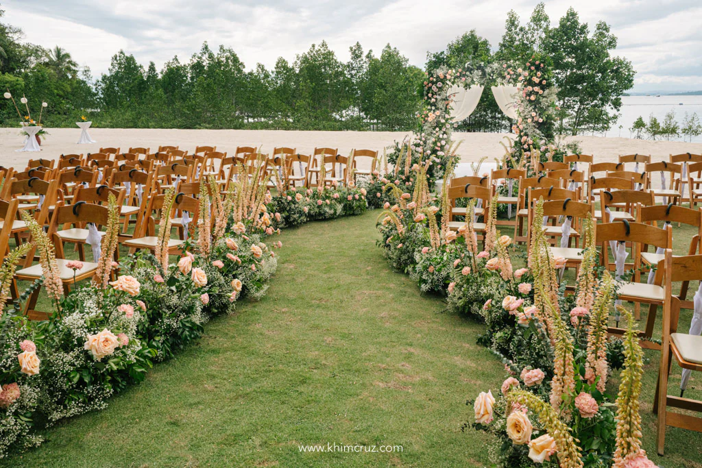 outdoor dreamy wedding ceremony of Uzziel and Patricia with floral pathway leading to floral arch entrance with beach front on the background