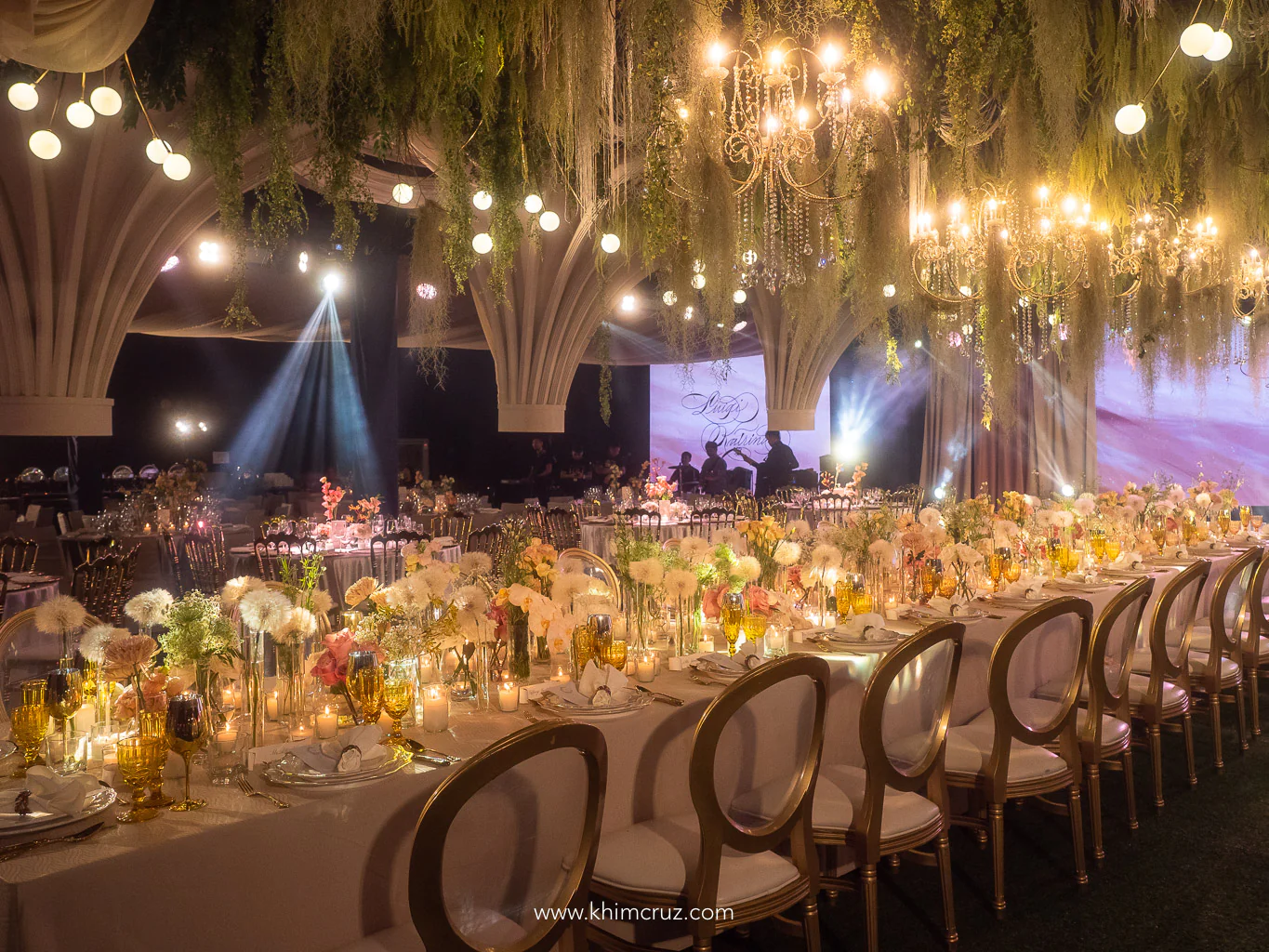 modern old-world hanging chandeliers with cascading greens above head table with floral centerpieces and candles