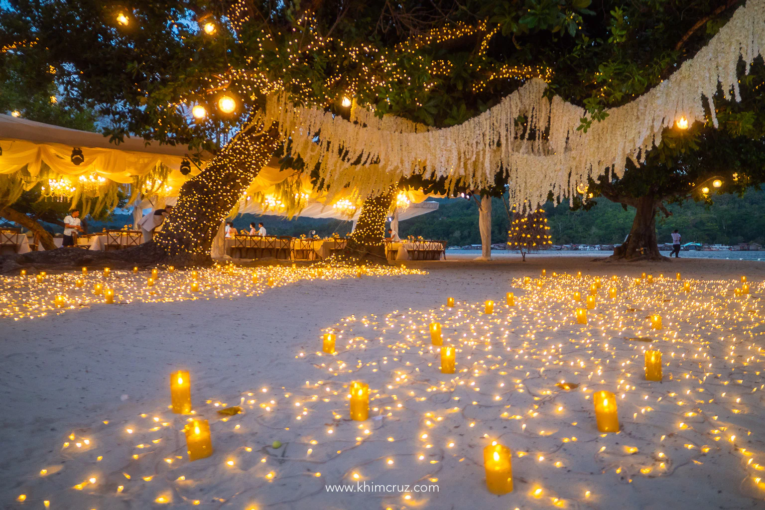 warm lights on trees and sand of beach lead the path to the wedding reception by Khim Cruz